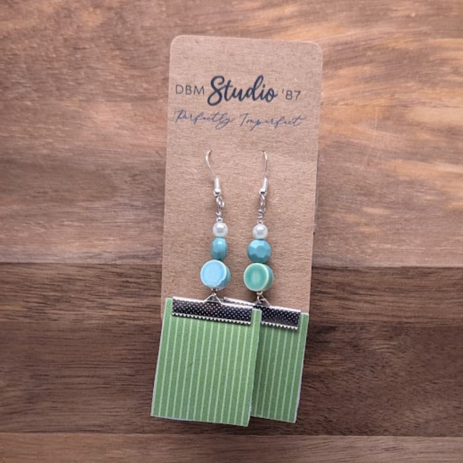 Earrings with white background blue flowered square front and green white stripe back with a few green/blue beads. Back is shown.