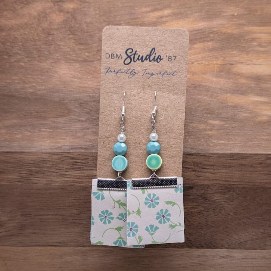 Earrings with white background blue flowered square front and green white stripe back with a few green/blue beads. Front is shown.