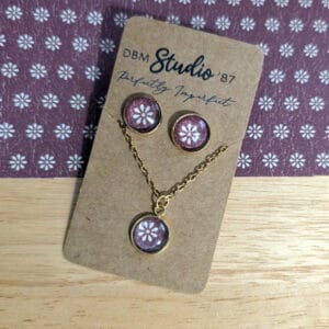 post earring and necklace set with glass cabochons, featuring a maroon background with a cream daisy sitting on a wooden table with coordinating paper
