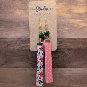 Long thin rectangle scrapbook earrings, with felt. Front light pink with red, yellow and green florals. Back is pink with light pink polka dots. Gold tone accents with Green and gold beads. Front and back are shown