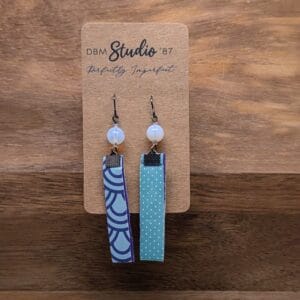 Medium length scrapbook earrings rectangles with purple felt core. Front is Light blue with purple swirls. Back is Light blue polka dots. Light blue/peal beads and pewter-toned metals. Back and front are shown